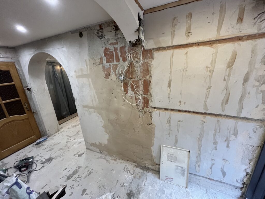 Prace murarskie i przygotowanie ścian pod tynki, widoczne łukowe przejście między pomieszczeniami.
